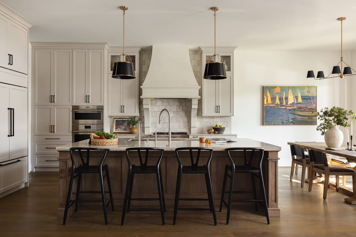 Kitchen island with black stools and pendant lighting open to the dining room