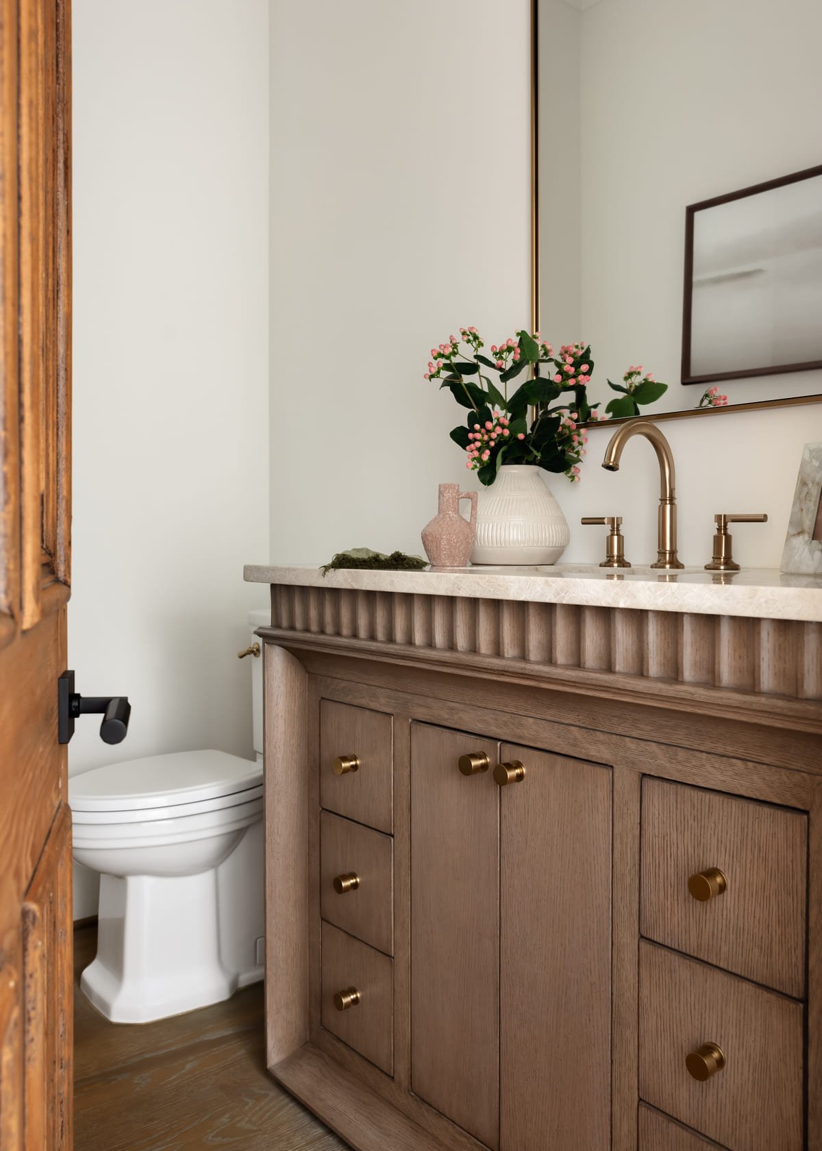 Powder room with an oak vanity, marble counter, and brass fittings