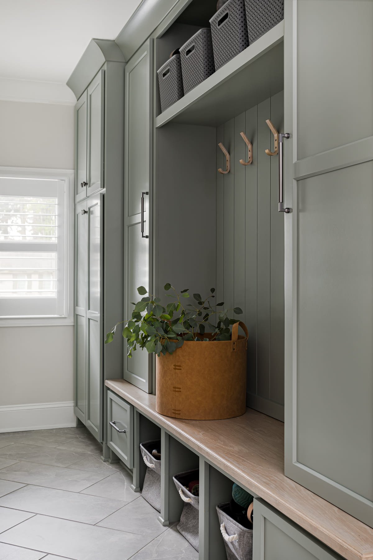 Sage green mudroom with tall lockers, a bench, and woven baskets