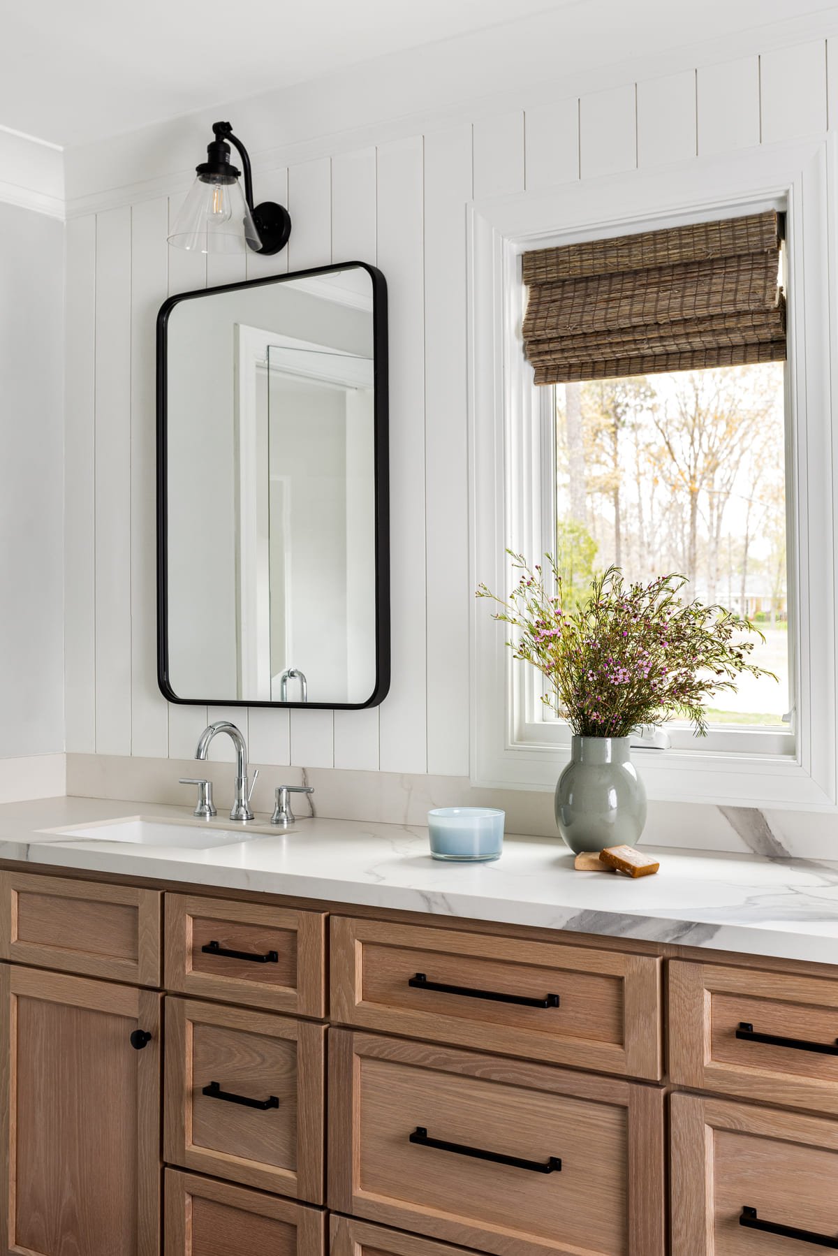 Single vanity with a black framed mirror and woven roman shade