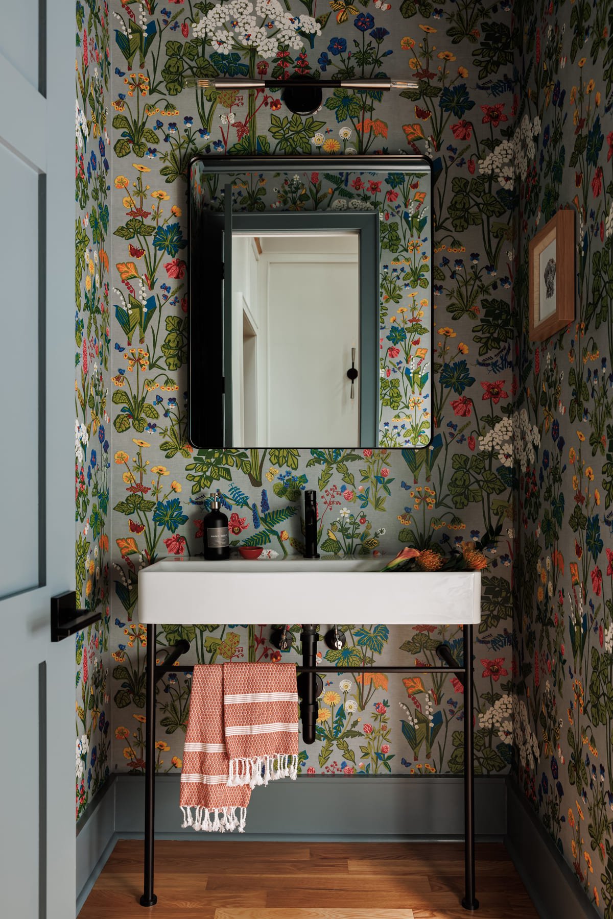 Powder room in full floral wallpaper with a floating stone sink
