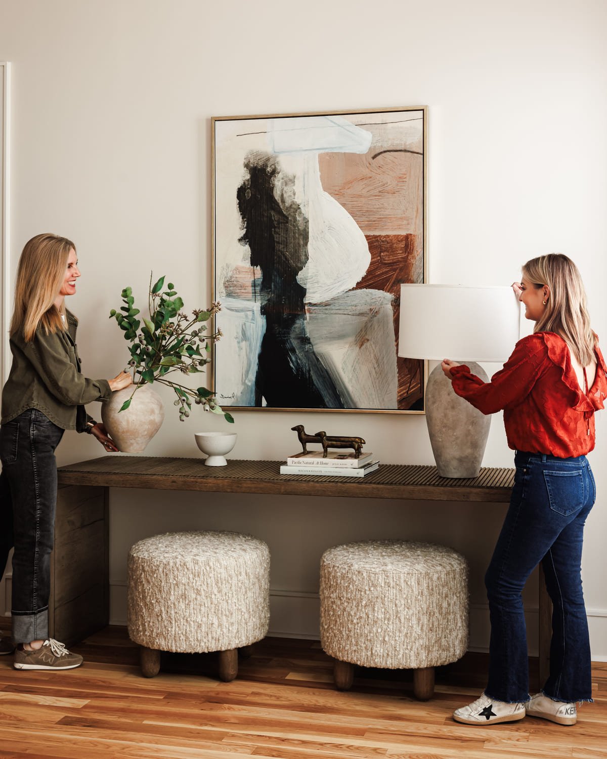 Two designers styling a console beneath a large abstract painting