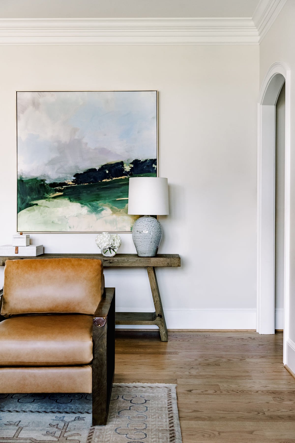 Landscape painting above a console with a caramel leather chair
