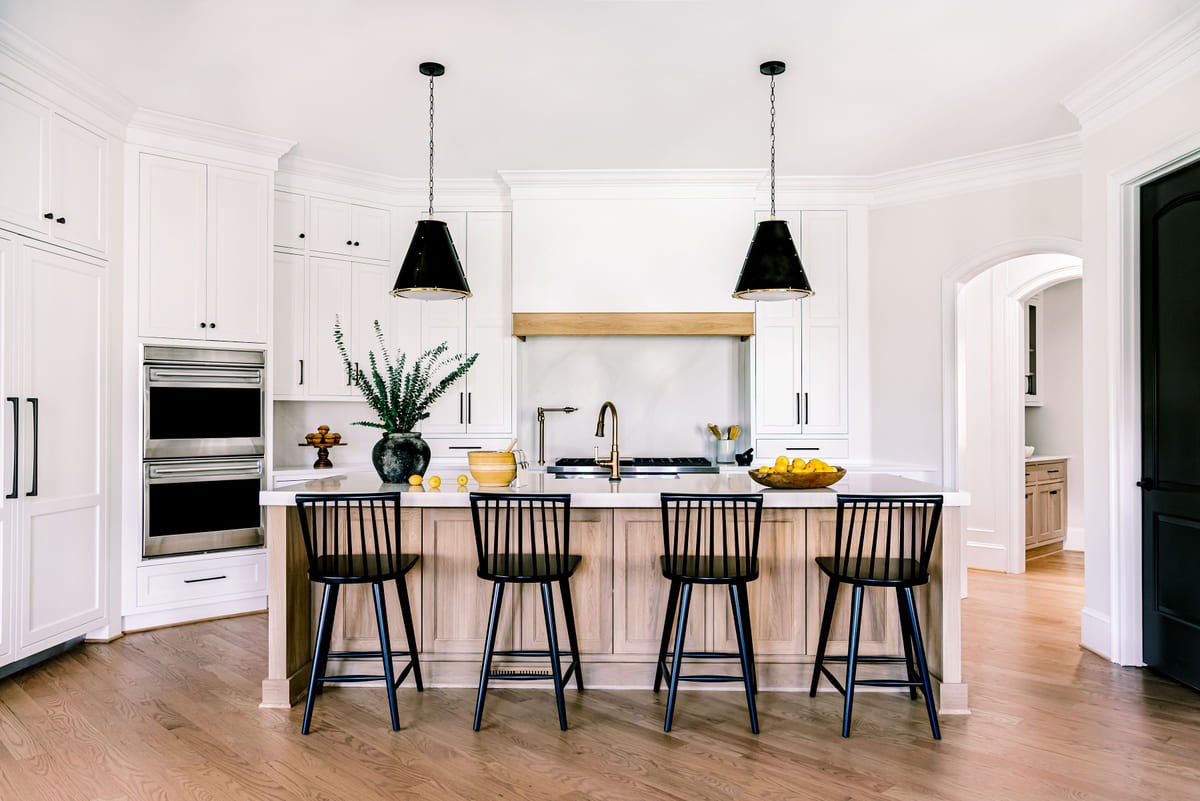Wide view of a white kitchen with black pendants and an oak island