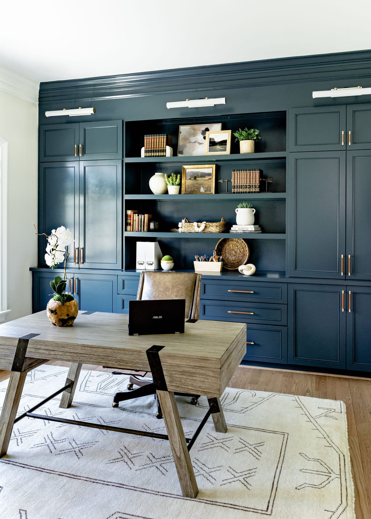 Navy built in office cabinetry with an oak desk and vintage rug