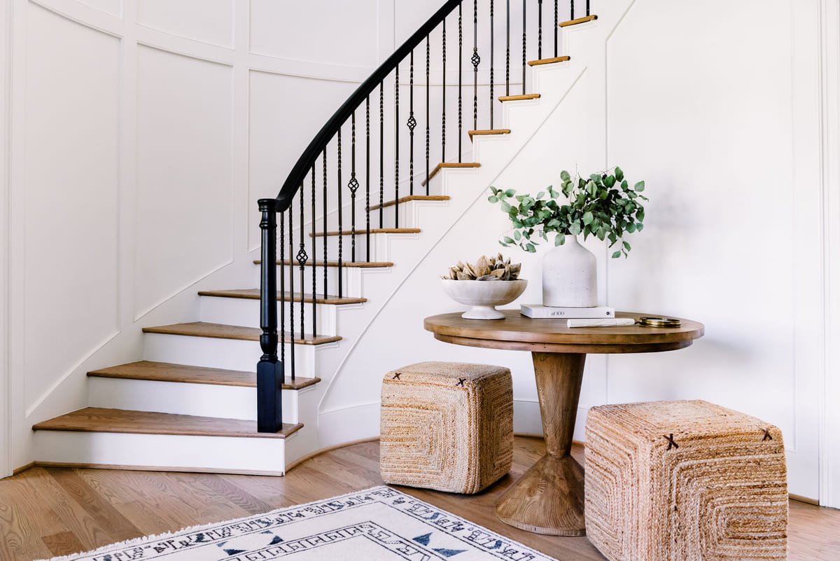 Curved staircase with a pedestal table and woven ottomans