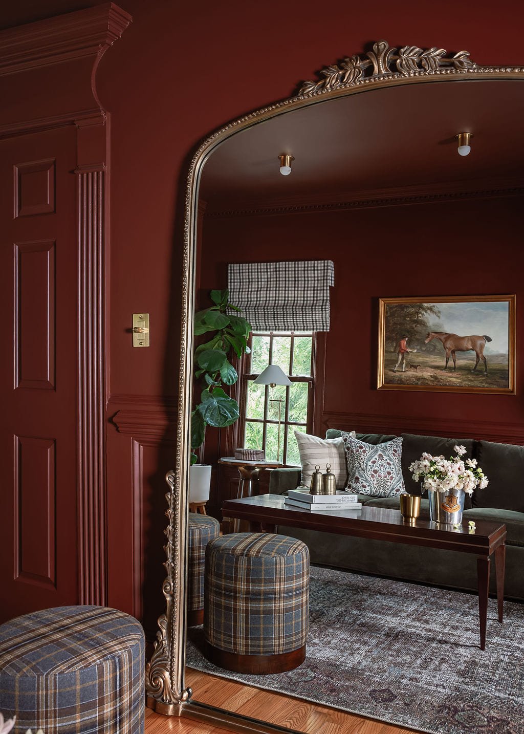 Oxblood lounge with an arched mirror and plaid upholstered ottomans