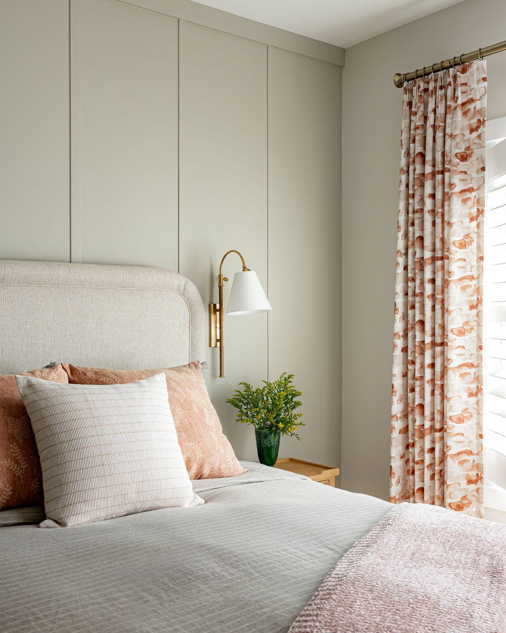 Primary bedroom with a brass swing arm sconce and floral drapery