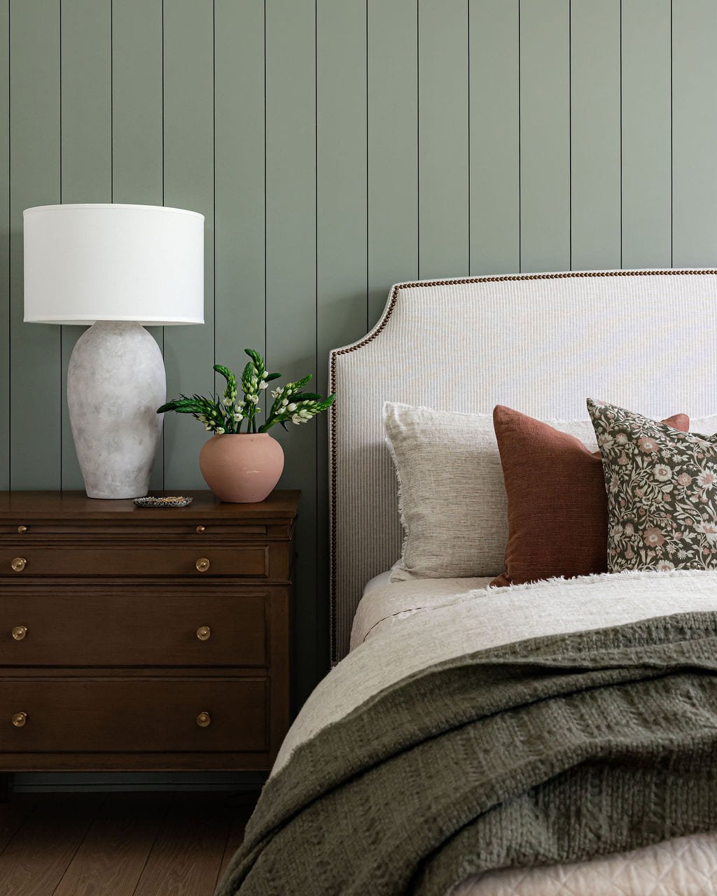 Bed against green board and batten paneling with an alabaster lamp