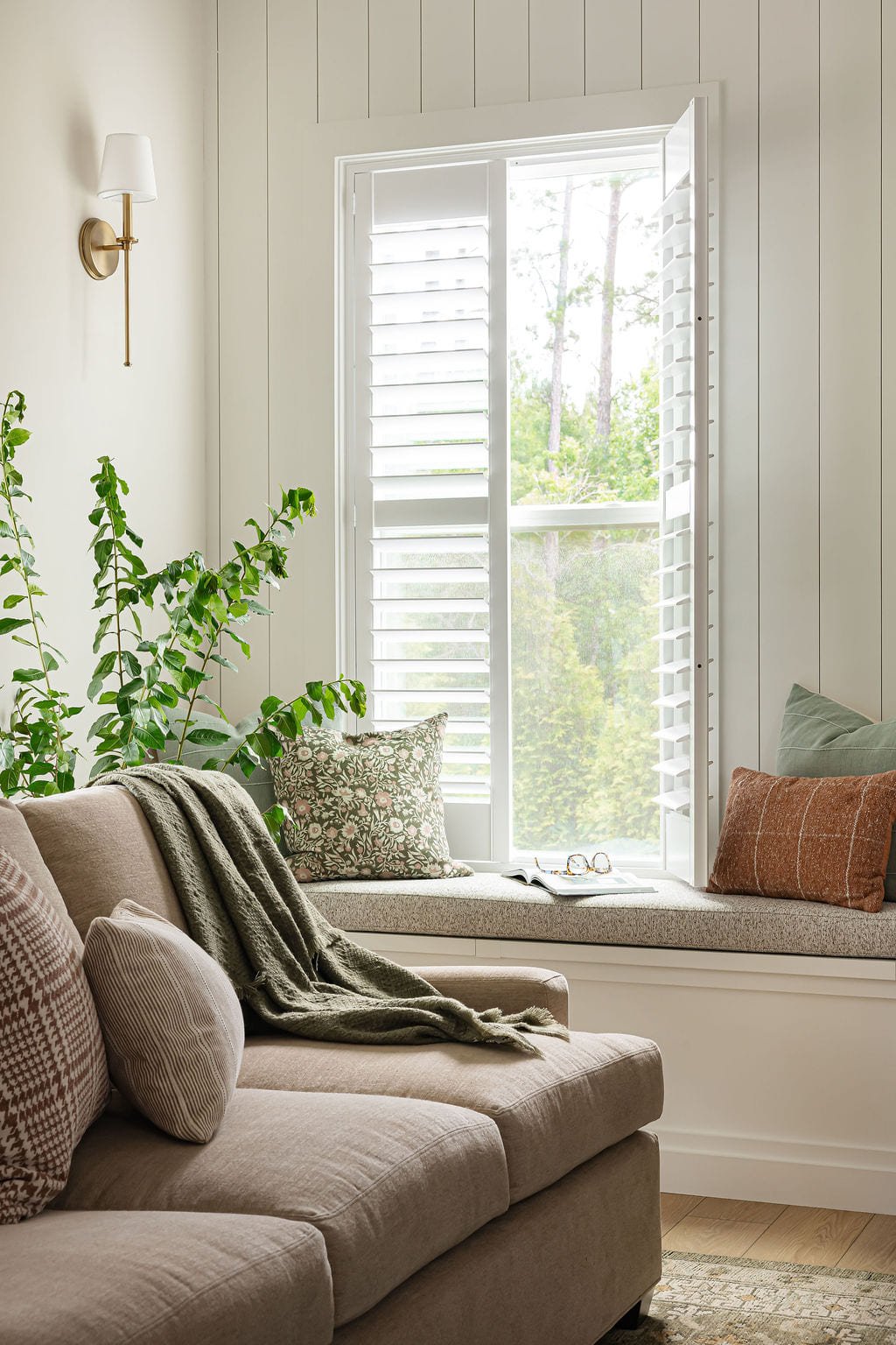 Window seat with a green throw beside plantation shutters