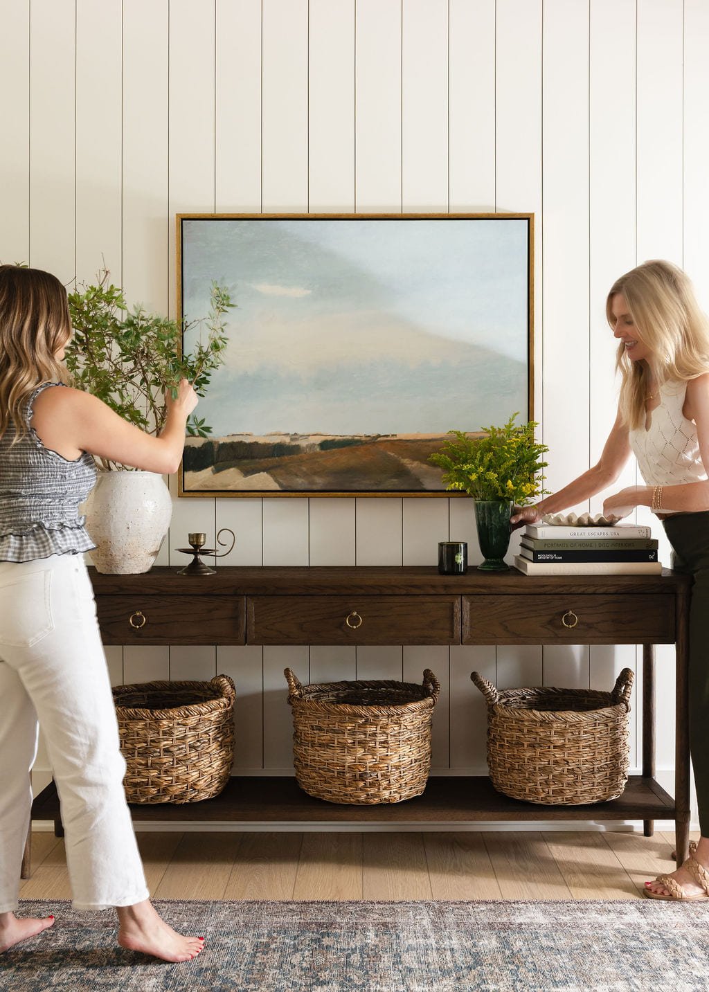 Designer styling a console table beneath a framed landscape