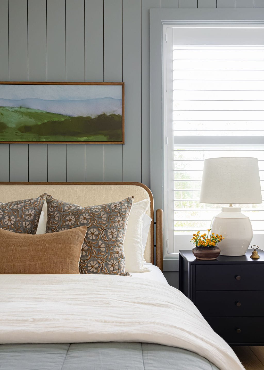 Bed layered in neutral linens with a carved wood nightstand