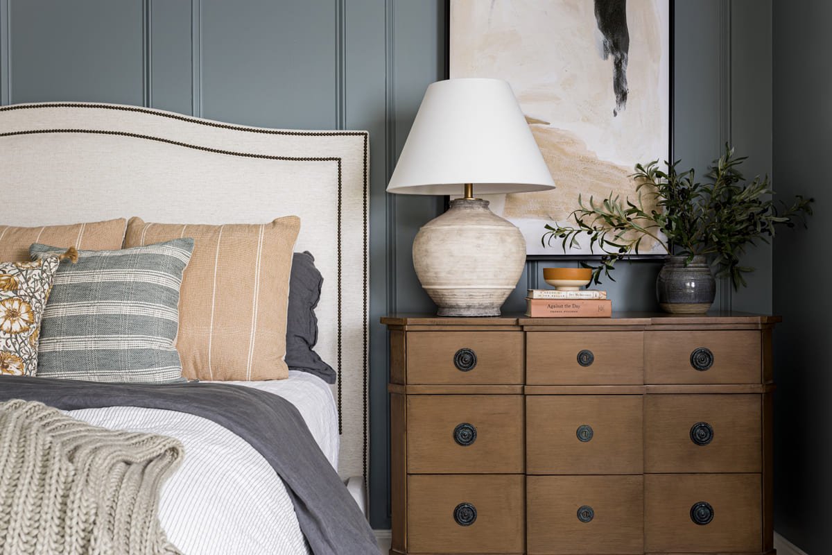 Primary bedroom with blue green paneling, an antique dresser, and an alabaster lamp