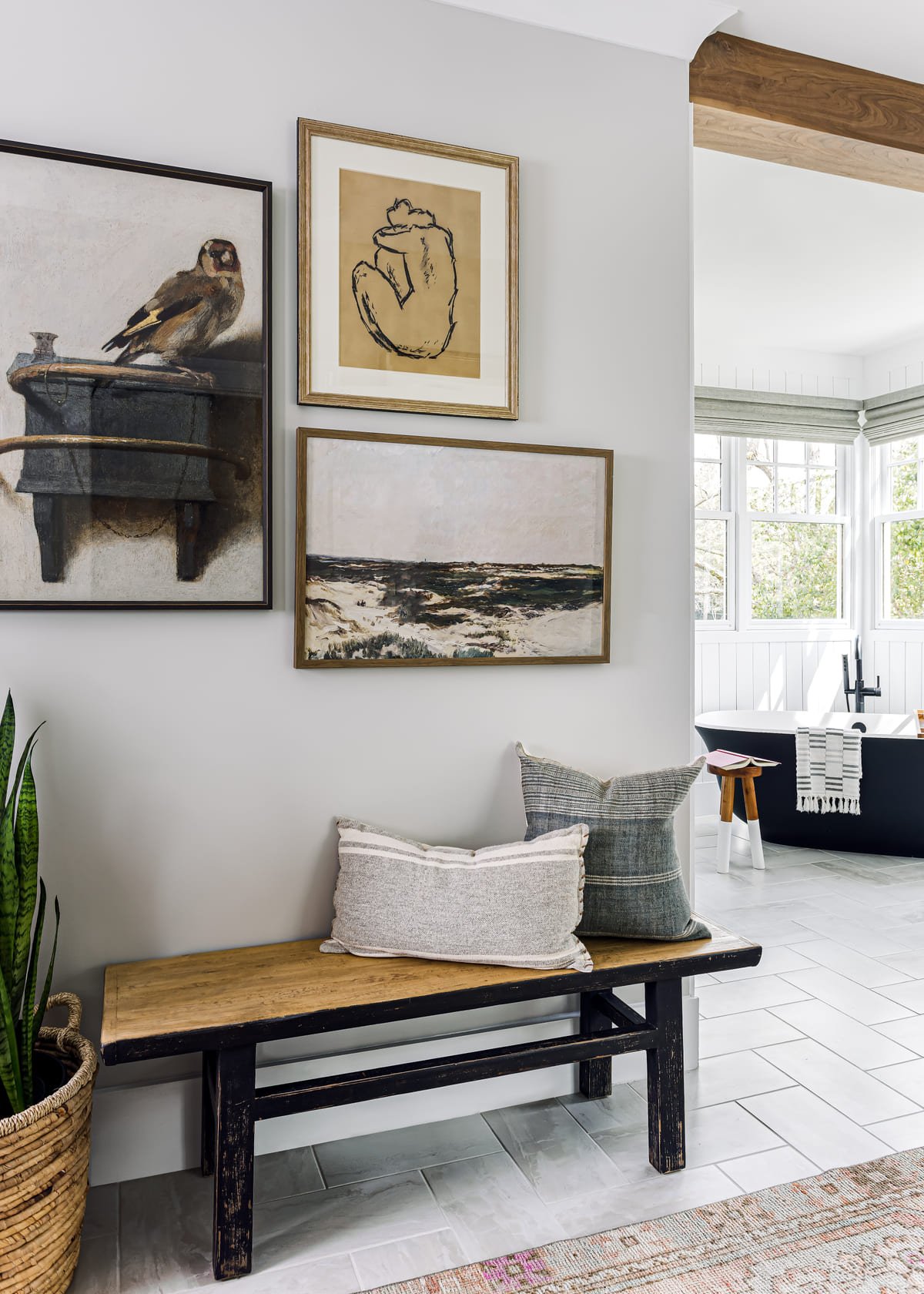Bench beneath layered framed art in a serene primary bedroom