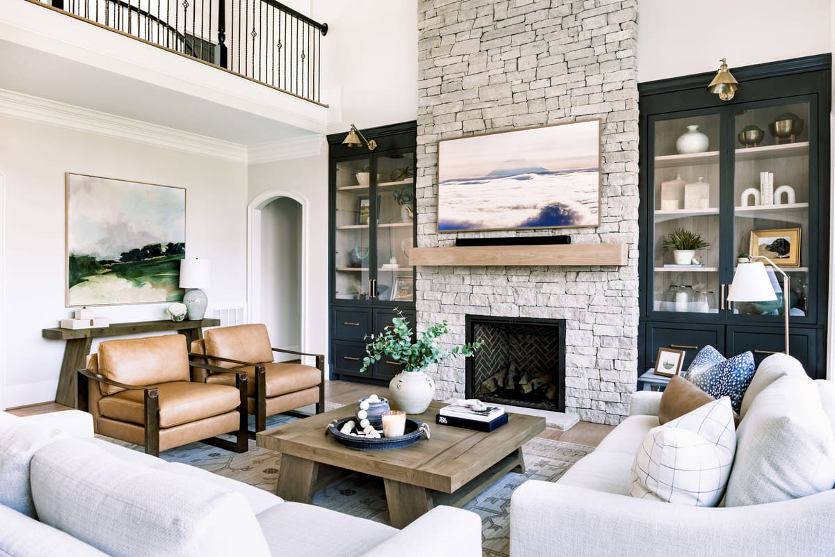 Two story living room with a stone fireplace, black cabinetry, and layered neutral seating, designed by Rebecca Driggs Interiors