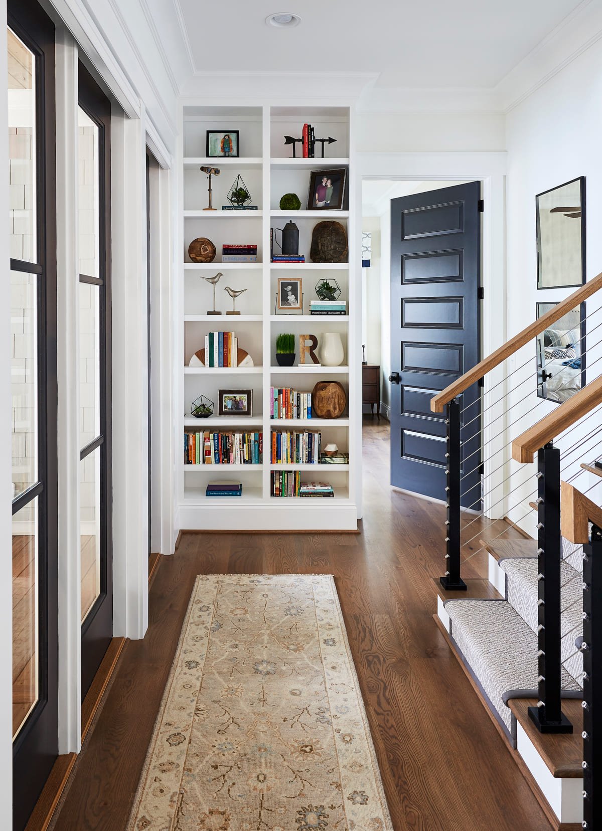 Hallway with built in bookshelves, a navy door, and a vintage runner