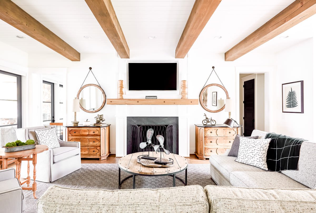Living room with exposed beams, a wood mantel, and paired round mirrors