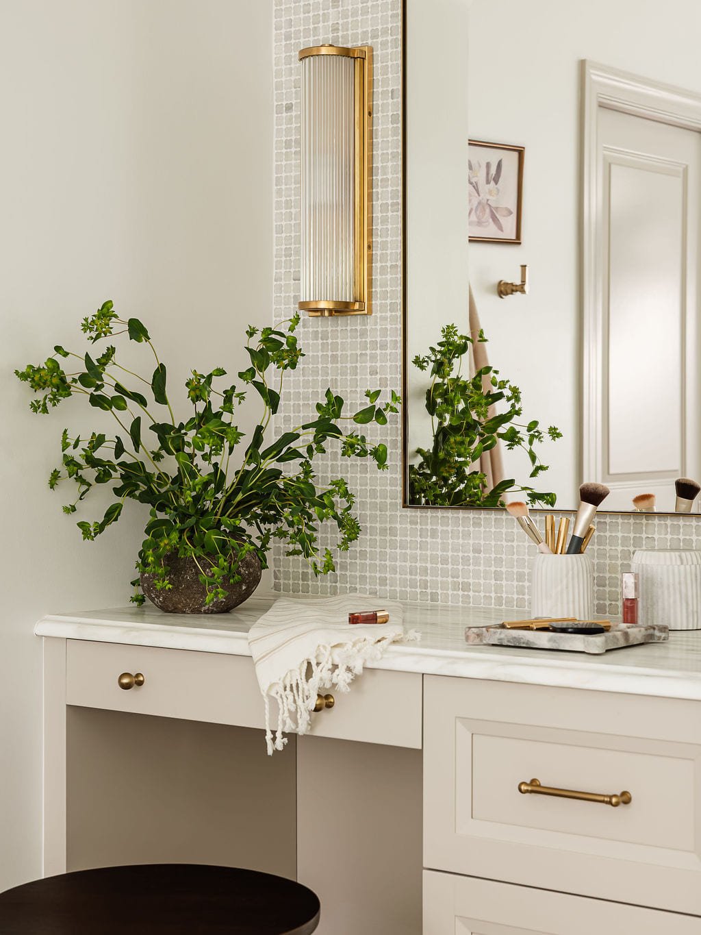 Makeup vanity with brass hardware, greenery, and a wall mounted mirror