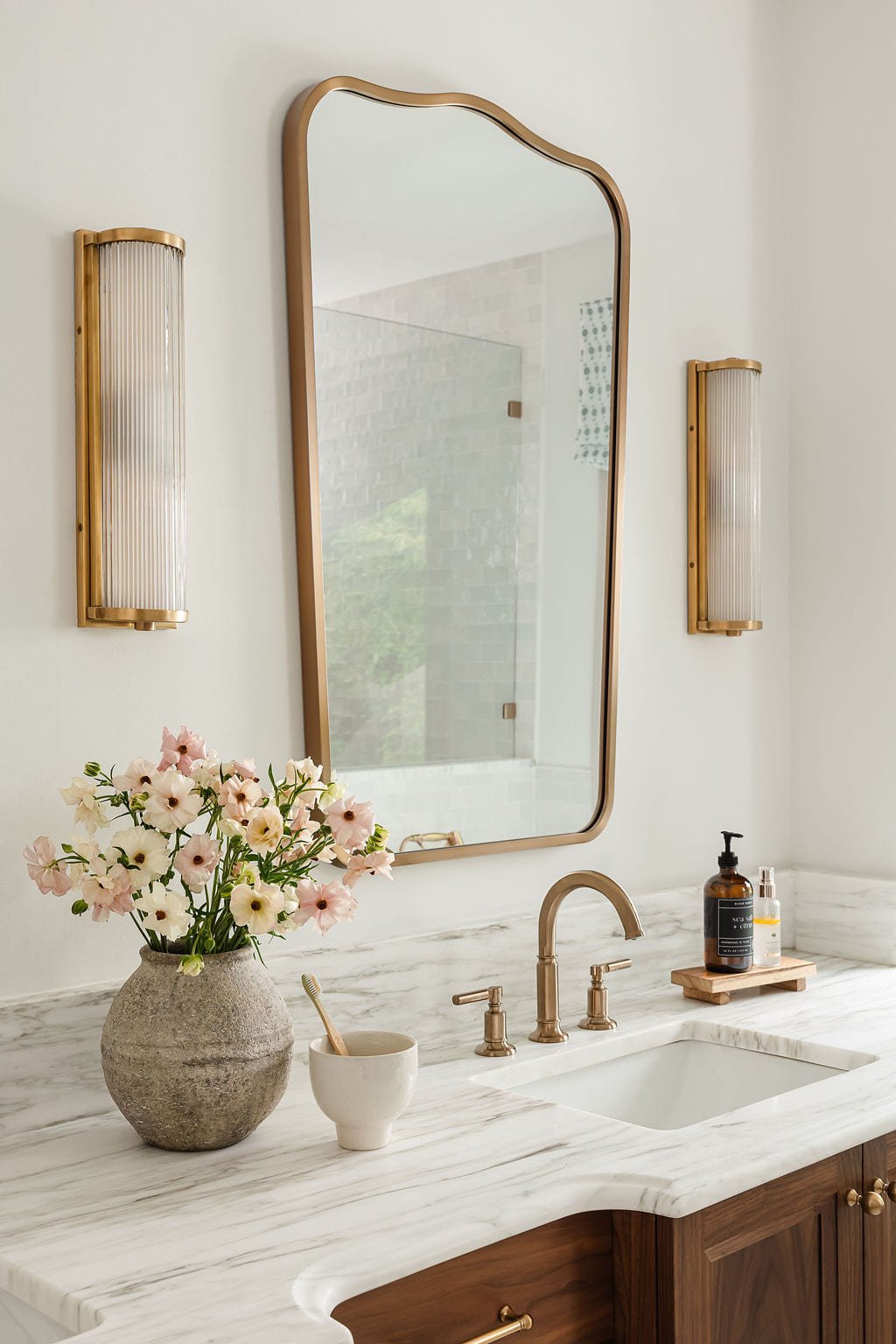 Marble double vanity with an arched brass mirror and fresh blooms