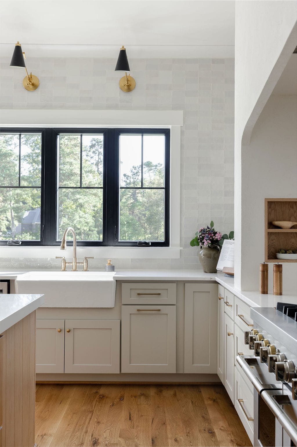 Sage green kitchen cabinetry with black steel windows and a farmhouse sink