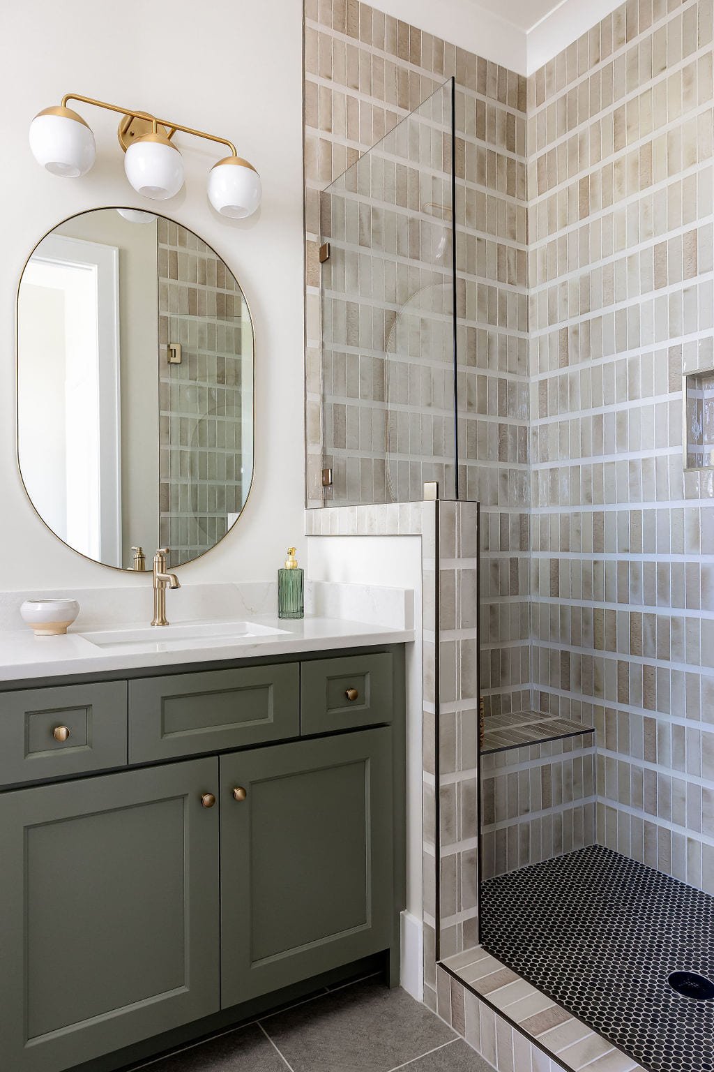 Bath with a sage vanity, oval mirror, and gray tiled shower