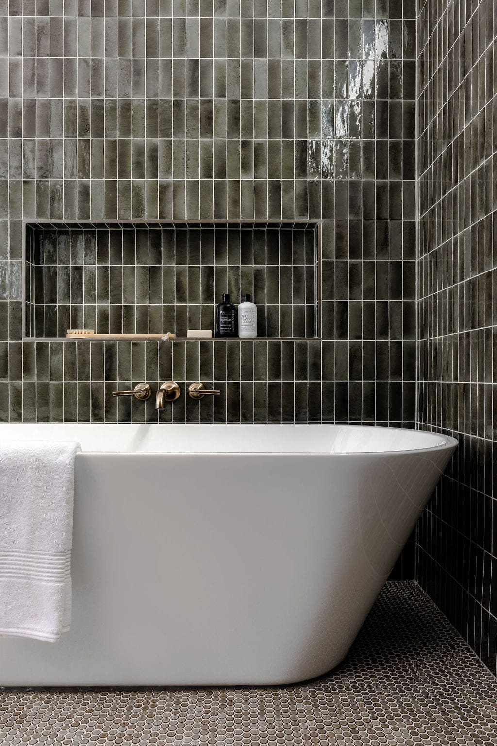 Freestanding soaking tub against a wall of dark green glazed tile