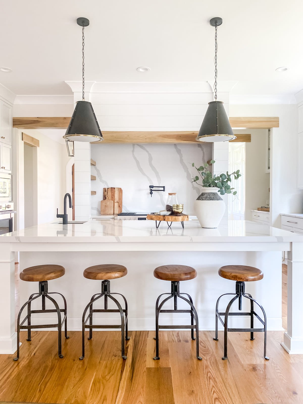 Kitchen island beneath a plaster hood with black pendant lighting