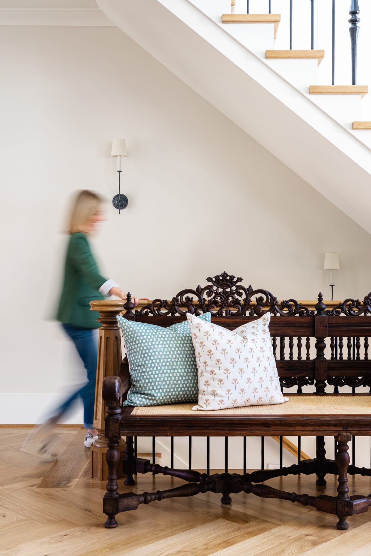 Carved antique bench beneath the staircase with layered pillows