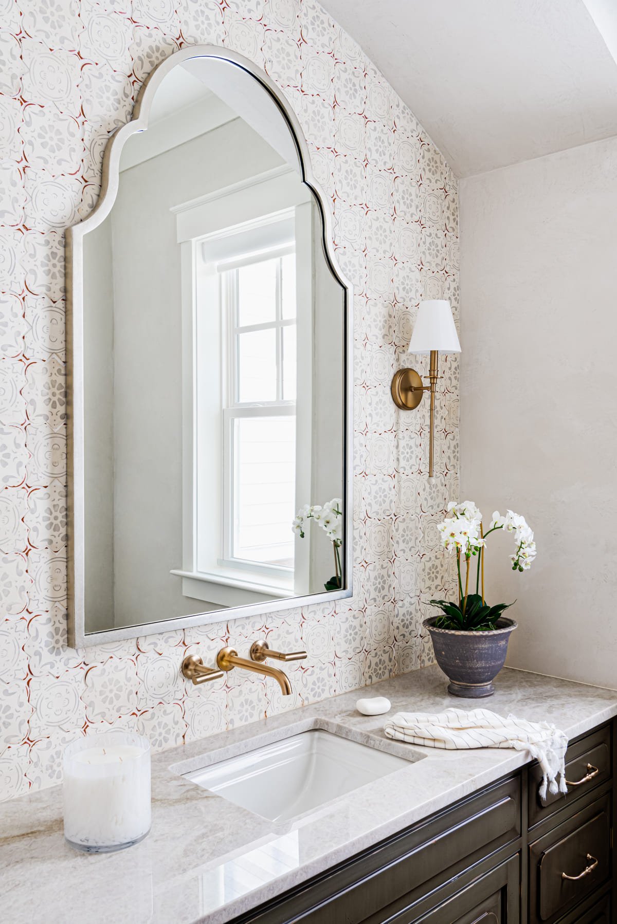 Powder room with an arched mirror and small scale patterned wallpaper